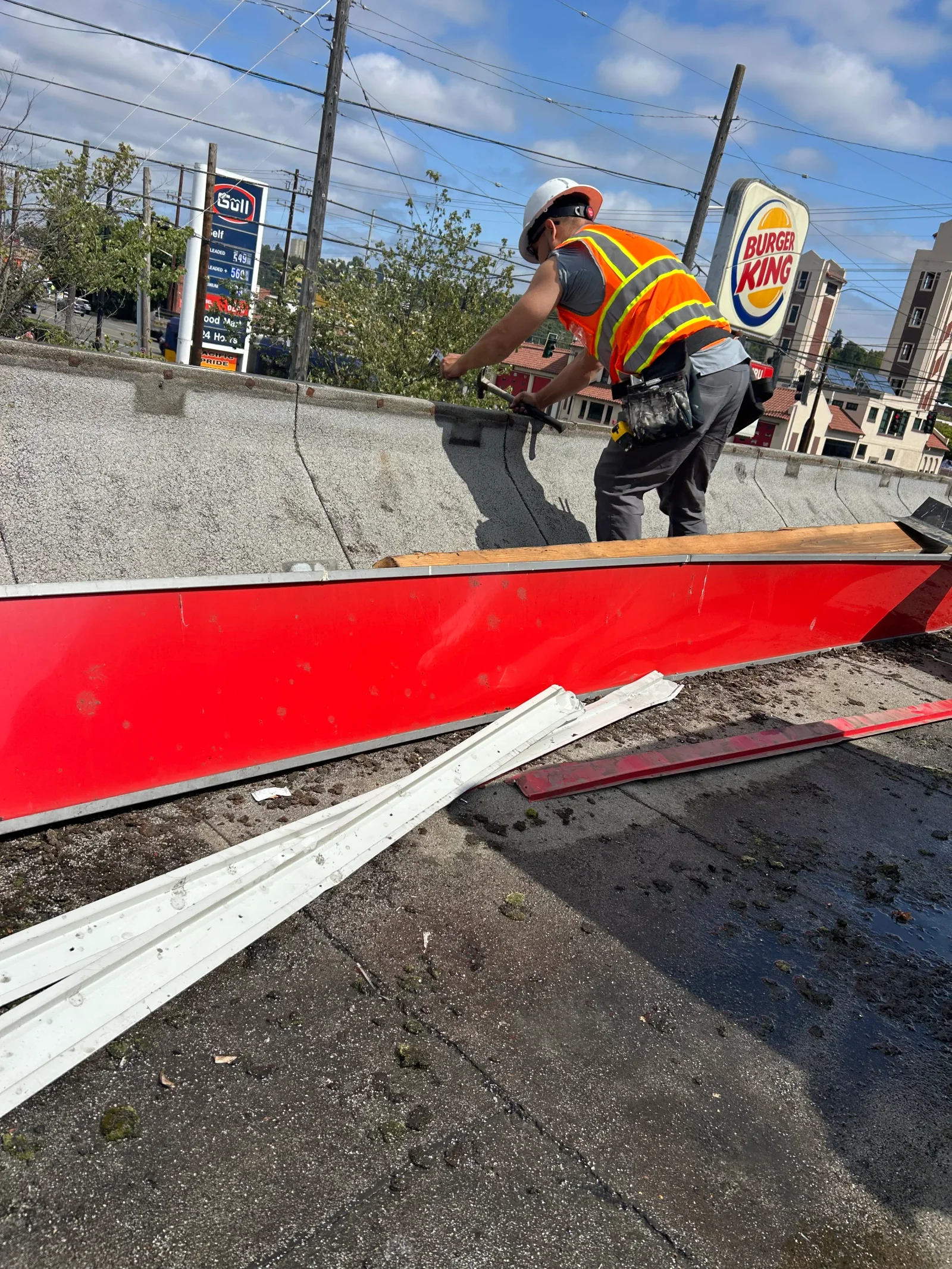 Worker installing red metal roofing panels with white trim on commercial flat roof
