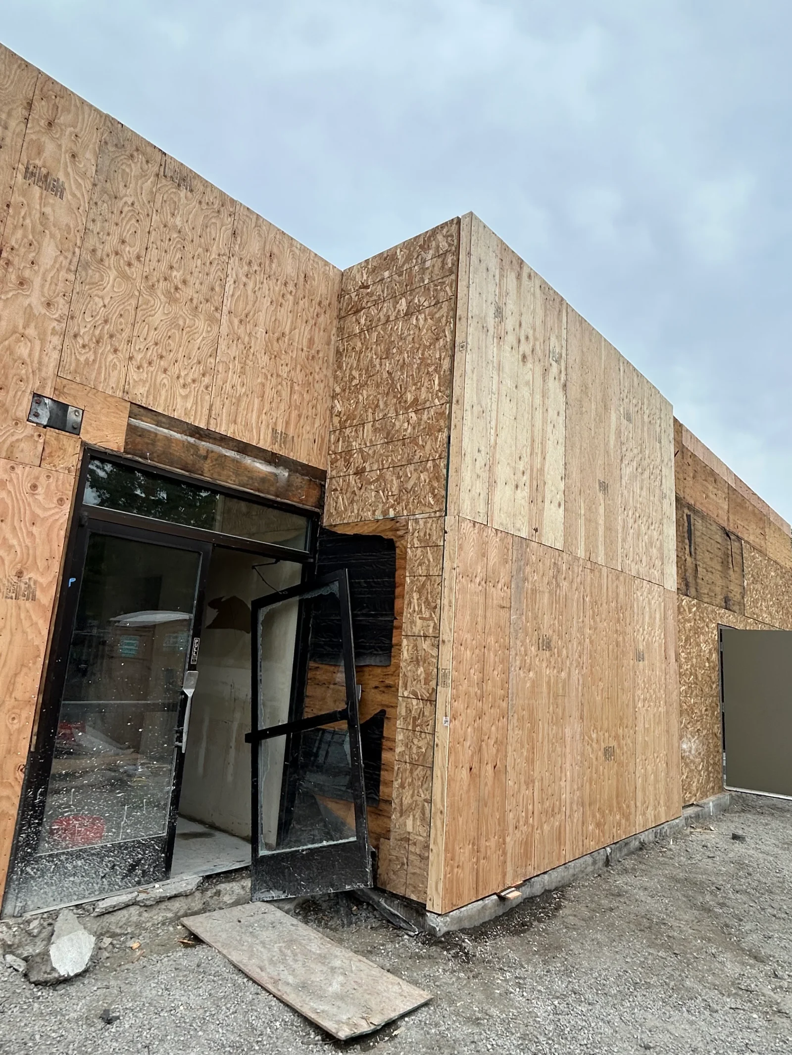 OSB-sheathed commercial structure with black-framed entry door and window opening