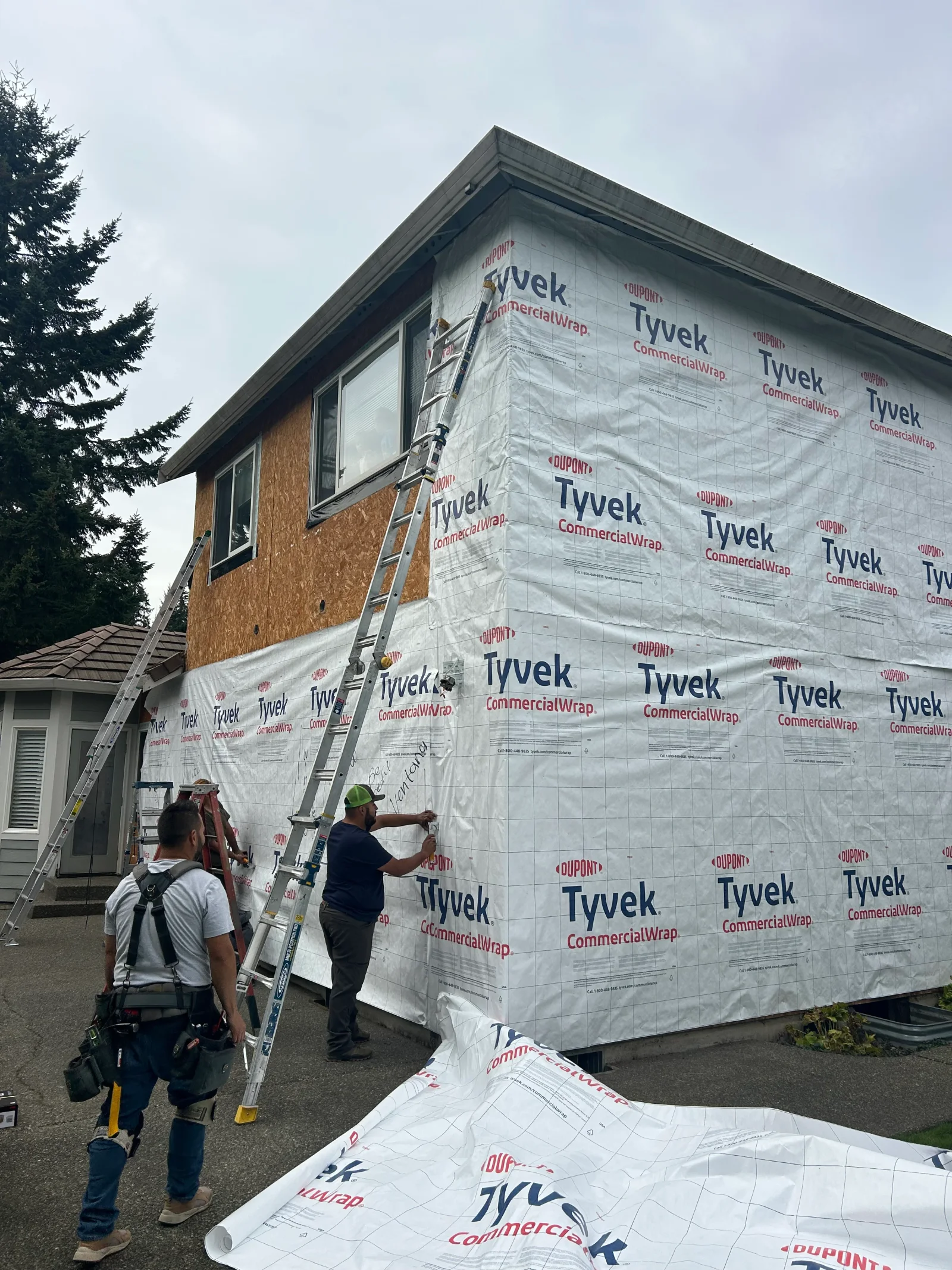 Tyvek house wrap installation on residential exterior with workers applying weatherproofing barrier