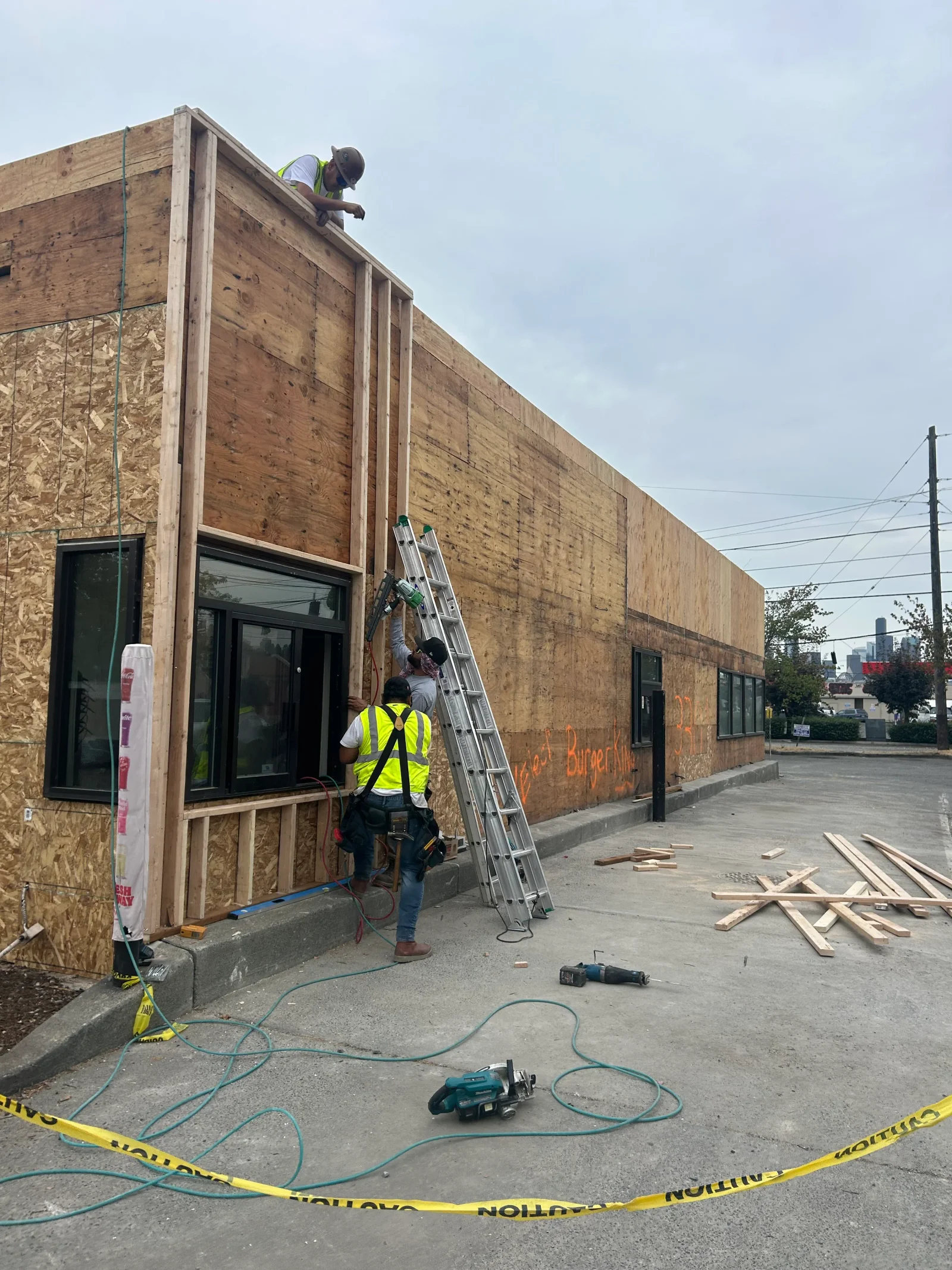 Commercial kitchen framing with OSB sheathing, black-framed windows, and workers on ladders during construction